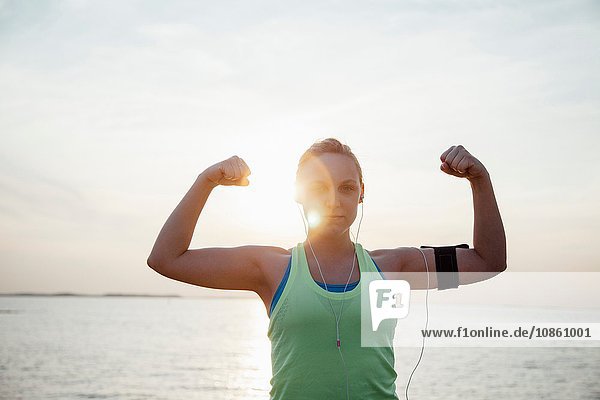 Woman wearing activity tracker  arms raised flexing muscles looking at camera