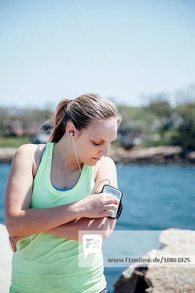 Woman wearing earbuds looking at activity tracker on arm