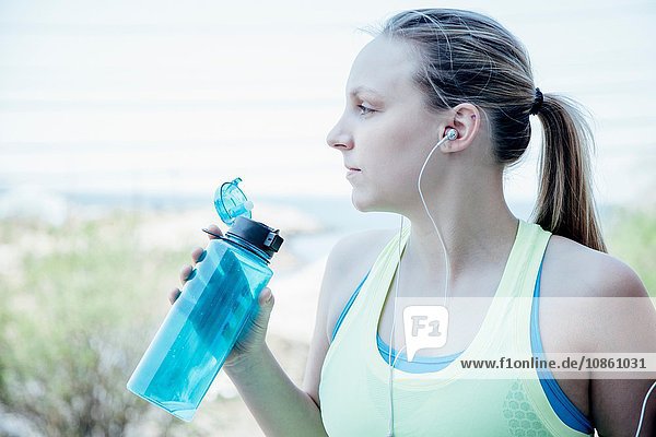 Frau mit Ohrstöpseln hält Plastik-Wasserflasche und schaut weg