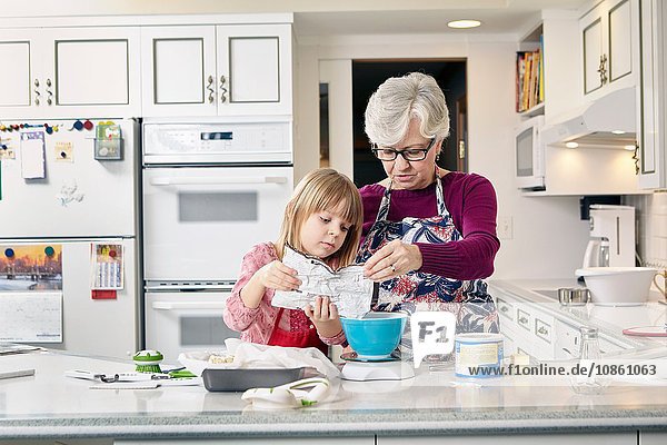 Mädchen und Großmutter gießen Kuchenmischung an der Küchentheke