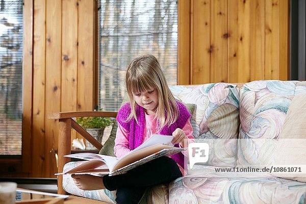 Mädchen sitzt und liest Geschichtenbuch auf Wohnzimmersofa