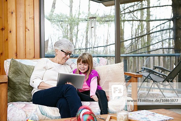 Ältere Frau und Enkelin durchsuchen digitales Tablet auf Wohnzimmersofa