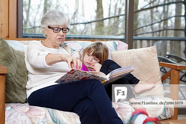 Ältere Frau liest Enkelin auf Wohnzimmersofa Geschichte vor