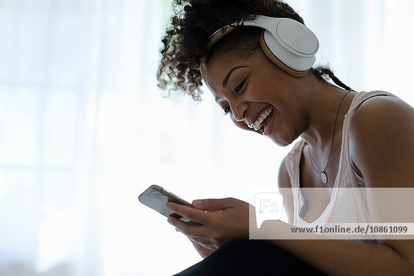Frau trägt Kopfhörer  schaut auf Smartphone  lacht