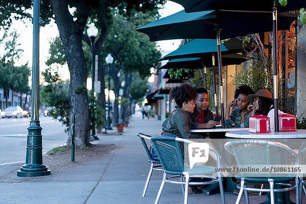 Gruppe von Freundinnen  die am Tisch sitzen  vor dem Café  mit Blick auf das Smartphone