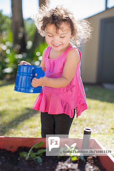 Junges Mädchen im Garten  hält Giesskanne  giesst Pflanzen in Kübel  lächelt