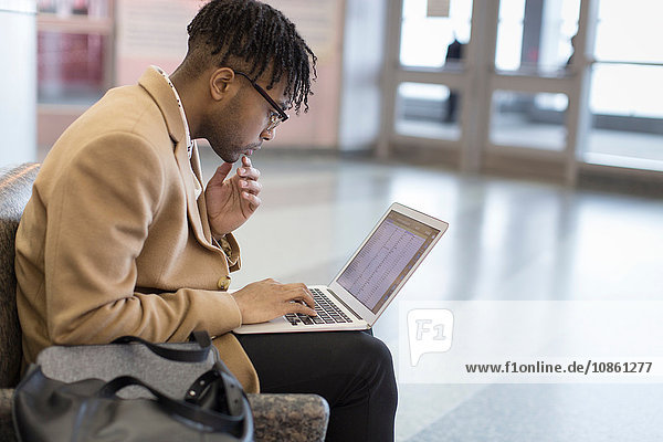 Young businessman sitting in train station typing on laptop