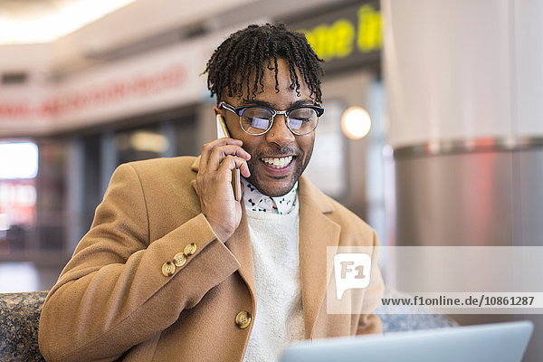 Junger Geschäftsmann sitzt im Bahnhof und spricht über Smartphone