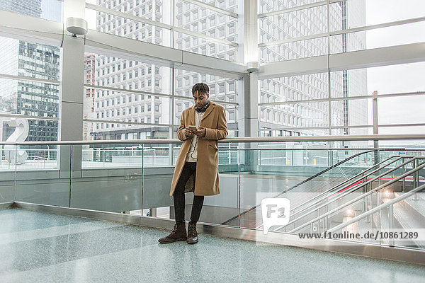 Junger Geschäftsmann wählt Smartphone-Musik im Atrium des Bahnhofs