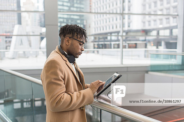Junger Geschäftsmann benutzt Touchscreen auf digitalem Tablet im Atrium des Bahnhofs