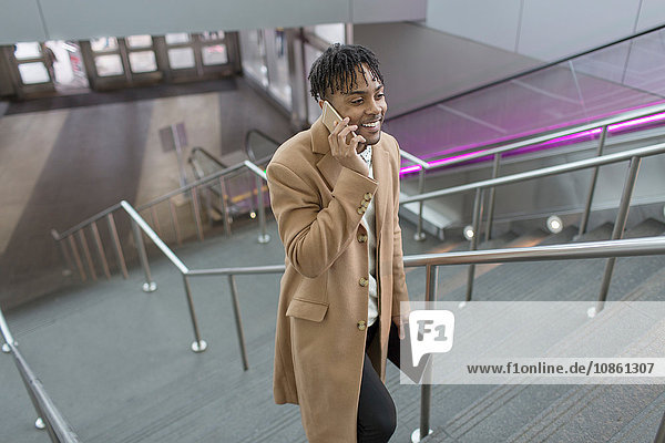 Junger Geschäftsmann im Gespräch auf Smartphone bewegt sich die Bahnhofstreppe hinauf