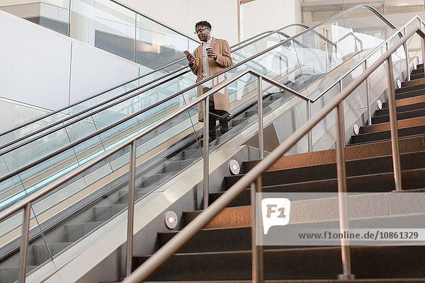 Young businessman moving down train station escalator with takeaway coffee
