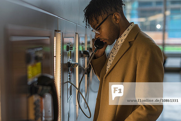 Serious young businessman talking on train station pay phone