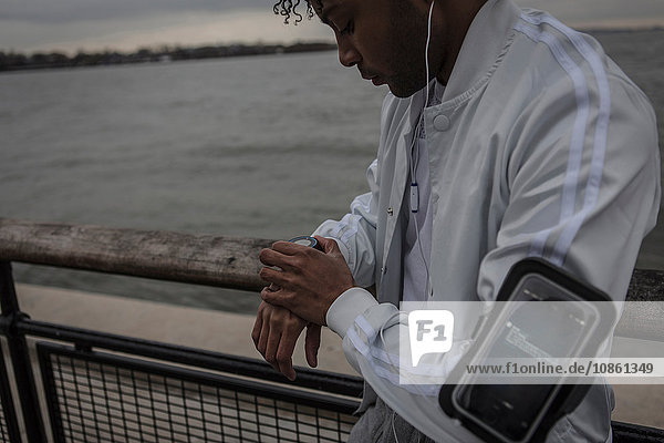 Junger Mann trainiert am Flussufer bei Tagesanbruch Zeitmessung auf Smartwatch