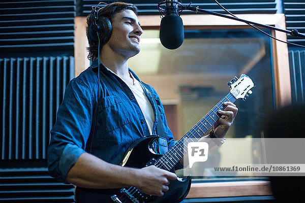 Männlicher Musiker im Aufnahmestudio  singt ins Mikrofon und spielt Gitarre