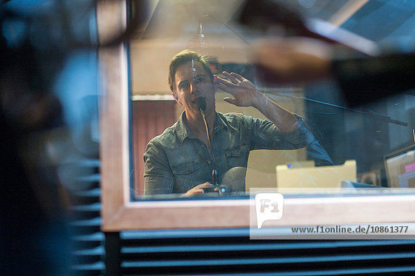 Musiker im Aufnahmestudio  Musikproduzent  der mit ihnen durch ein Fenster kommuniziert