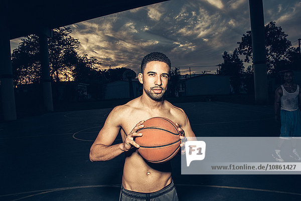 Bare chested man on basketball court holding basketball looking at camera