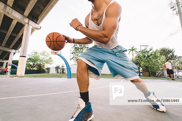 Cropped view of man on basketball court running bouncing basketball