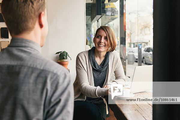 Over shoulder view of man chatting to woman at coffee shop window seat