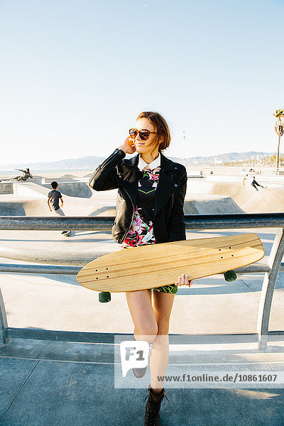 Junge Frau steht an der Reling  in der Nähe des Skateparks  hält Skateboard