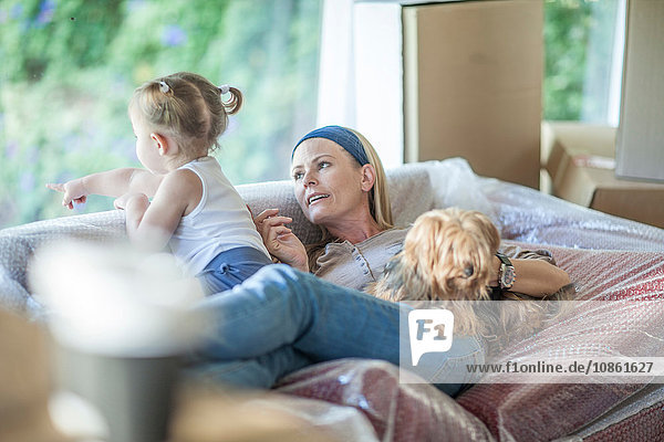 Umzug: Muttertochter und Haushund entspannen sich auf einem Sofa mit Luftpolsterfolie