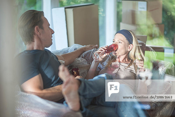 Umzug: Paar entspannt sich auf einem mit Seifenblasen umhüllten Sofa  in einem Zimmer mit Pappkartons  trinkt aus Champagnerflöten