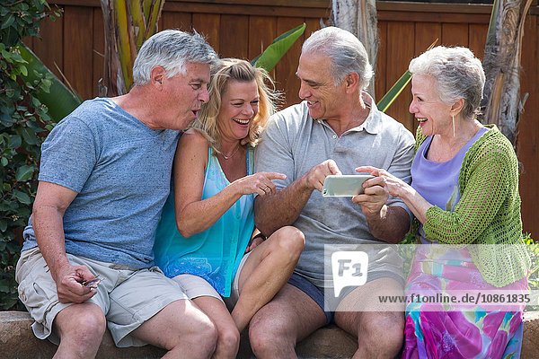 Gruppe von Senioren  die am Pool über Fotos in Smartphones lachen