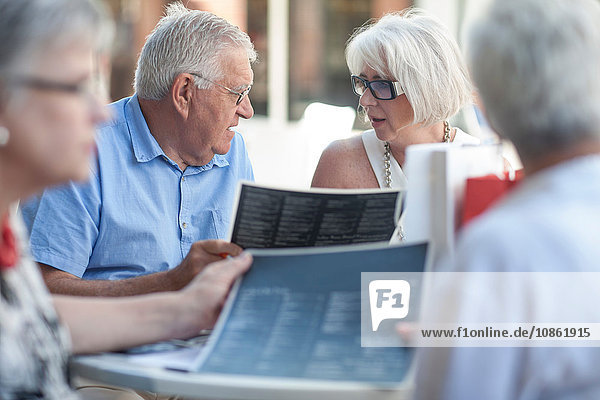 Älterer Mann und reifere Frauen lesen Speisekarten im Straßencafé
