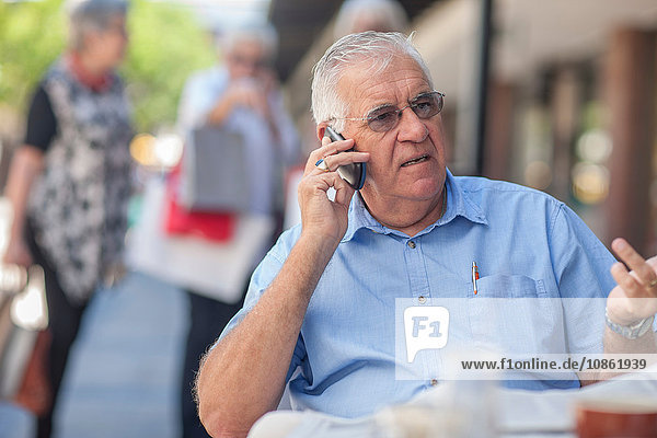 Älterer Mann sitzt vor einem Café und benutzt ein Mobiltelefon