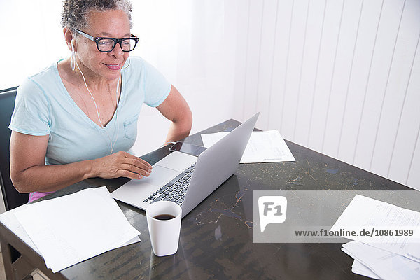 Senior woman sitting at table  using laptop  paperwork on table