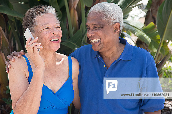Senior couple sitting outdoors  using smartphone  smiling