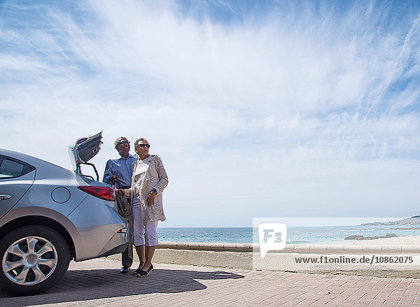 Älteres Ehepaar steht mit offenem Kofferraum neben dem Auto  in Strandnähe