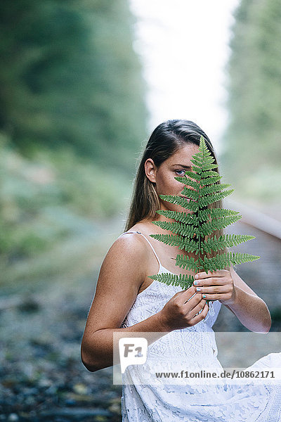 Teenager-Mädchen  sitzt im Freien  hält Pflanze vor dem Gesicht