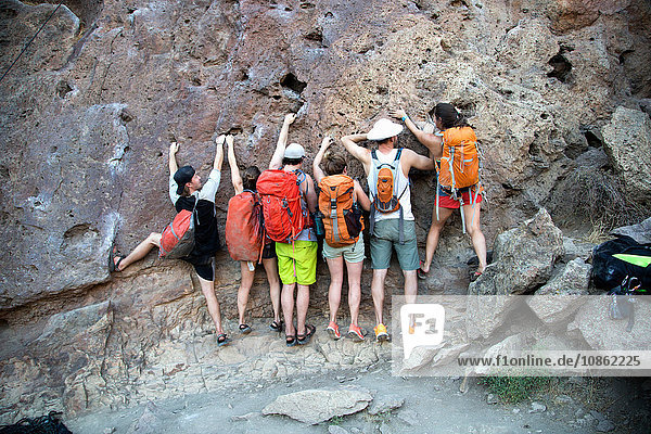Rear view of group of friends side by side clinging onto rock face