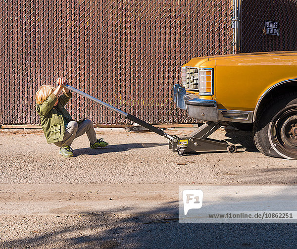 Junge benutzt Wagenheber zum Anheben eines Autos