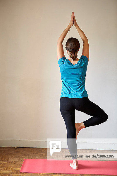 Rückansicht einer Frau auf einem Bein  Arme in Yogastellung erhoben