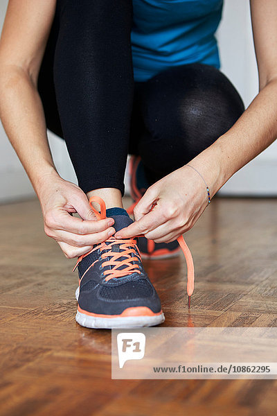 Low section of woman crouching tying shoelace on running shoe