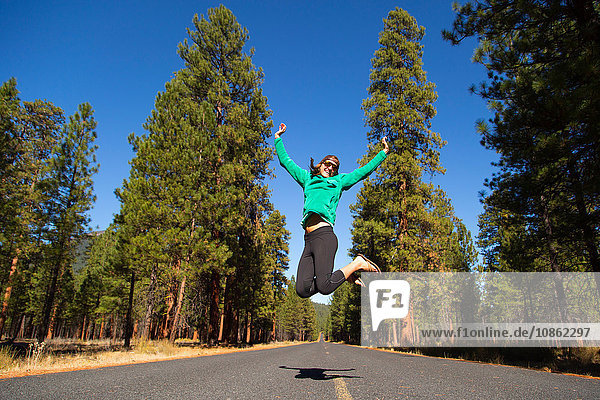 Young woman jumping mid air on forest road  Sisters  Oregon  USA