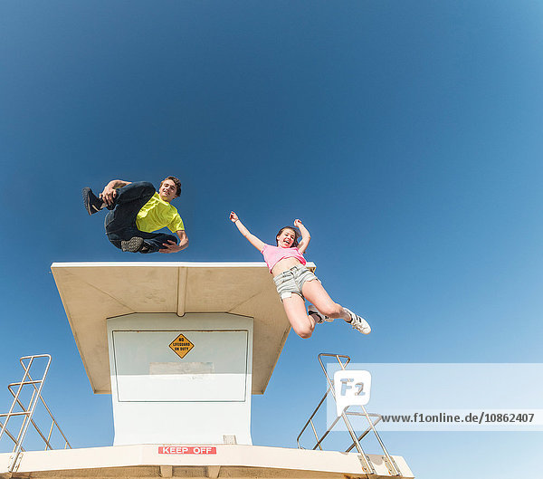 Paar springt in die Luft neben dem Rettungsschwimmerturm