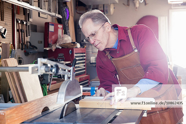 Senior man sawing woodblock in carpentry workshop