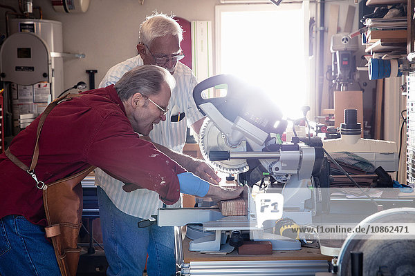 Senior men sawing woodblock on circular saw in carpentry workshop