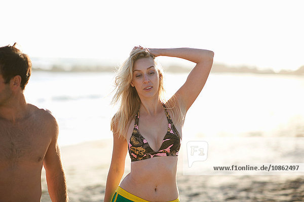 Frau am Strand im Bikini-Oberteil  die Hand im Haar nach unten blickend