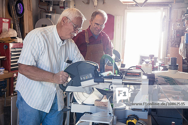 Senior men sawing woodblock in carpentry workshop
