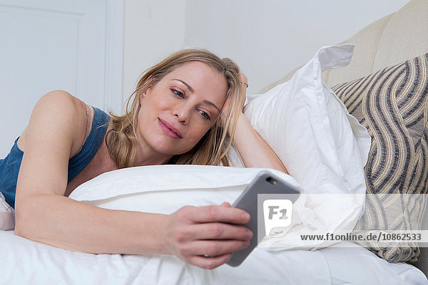Frau im Bett liest Smartphone-Texte