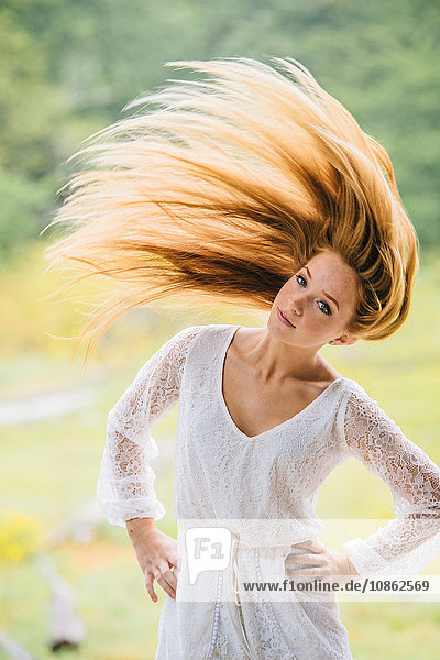 Portrait of teenage girl shaking head of long red hair in park