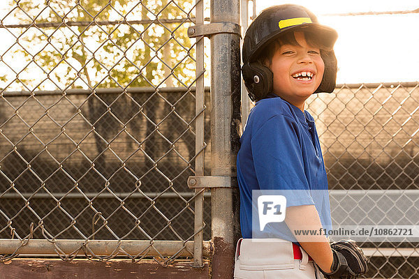 Laughing boy leaning against fence at baseball practise