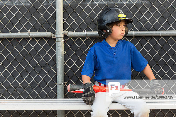 Junge mit Baseballschläger schaut beim Baseball-Training von der Bank aus zu