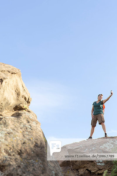 Wanderfrau steht auf Felsen und benutzt Smartphone zur Selbsthilfe