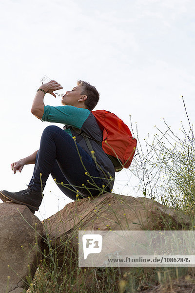 Wanderfrau sitzt auf Felsen und trinkt Wasser aus Flasche