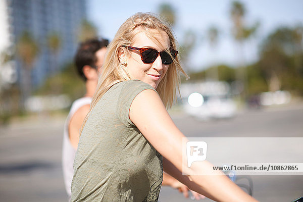 Young woman looking over her shoulder whilst cycling with boyfriend at Venice Beach  Los Angeles  California  USA